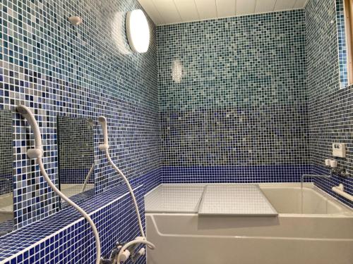 uma casa de banho em azulejos azuis com uma banheira e um espelho. em Ichinokurasou em Hakuba