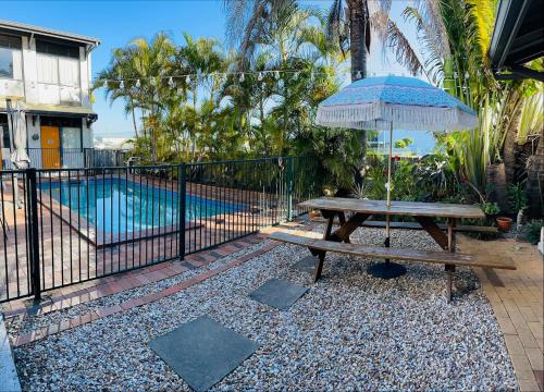 YHA Coolangatta Gold Coast في غولد كوست: طاولة نزهة مع مظلة بجوار حمام السباحة