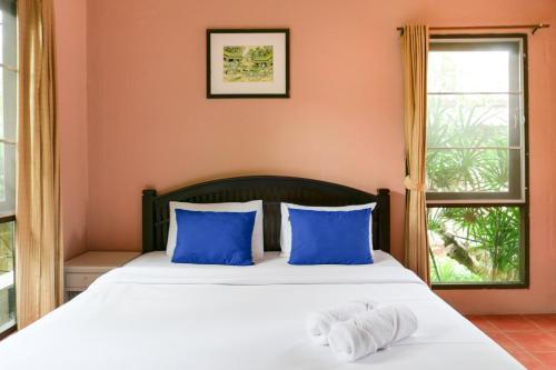 a bedroom with a bed with blue pillows and a window at Flora Ville-SHA PLUS in Chalong
