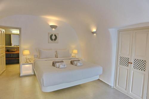 a white bedroom with a large white bed with two pillows at Oia Mare Villas in Oia