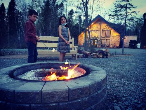 Ein Junge und ein Mädchen stehen neben einer Feuerstelle in der Unterkunft Maplebrook Retreat in Pointe-du-Chêne