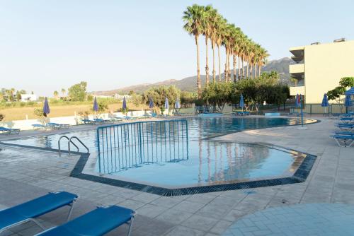 a swimming pool with blue chairs and palm trees at Oasis Tigaki in Tigaki