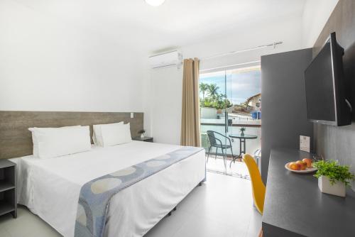 a bedroom with a bed and a balcony with a table at Hotel Cajueiro Guarujá in Guarujá