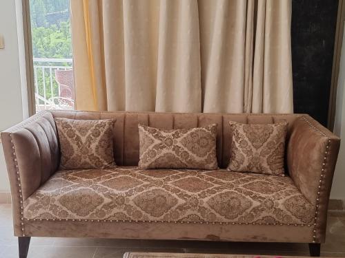 a brown couch with pillows in front of a window at Srinagar Homes in Muzaffarabad