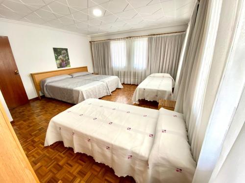 a hotel room with two beds with white sheets at Garden Lodge Hostal Evencio in Ribadavia