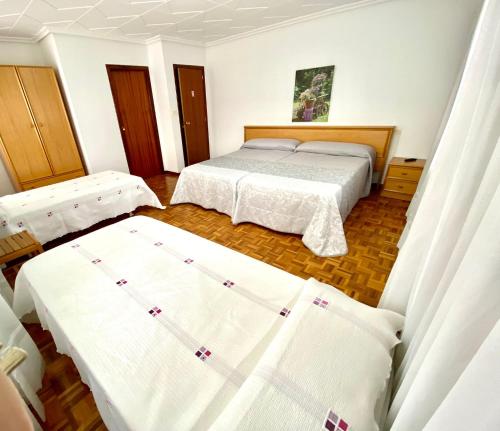 two beds in a room with white sheets at Garden Lodge Hostal Evencio in Ribadavia