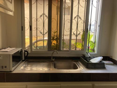 a kitchen sink with a microwave and a window at Chez Camille a Zac Mbao in Diokoul