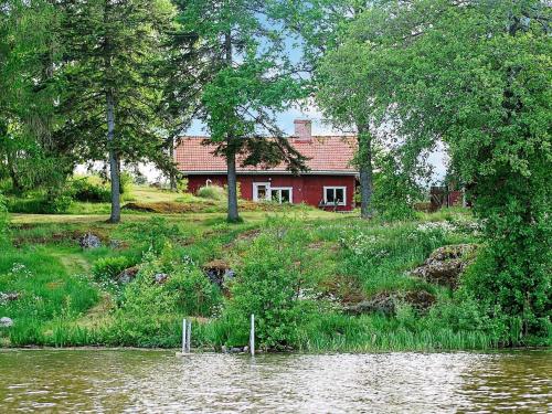 エスキルストゥーナにある6 person holiday home in ESKILSTUNAの川の横の丘に腰掛けた赤い家