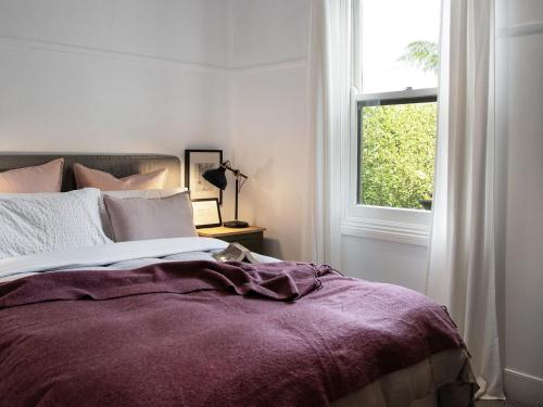 1 dormitorio con 1 cama con manta morada y ventana en Wombat Hill Cottage, en Daylesford