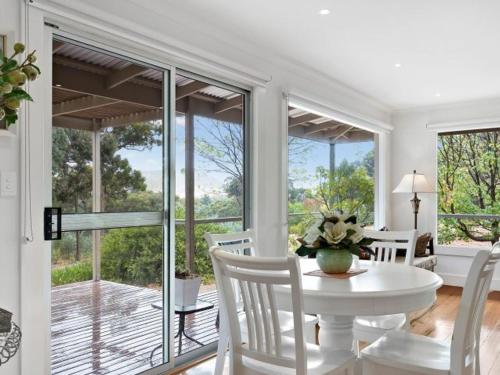 a dining room with a white table and chairs and windows at Margies on Mt Franklin 8 minutes from Daylesford in Hepburn Springs