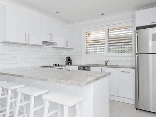 a white kitchen with white appliances and white stools at Burraneer at Corlette in Corlette