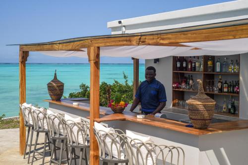 a man standing at a bar with chairs at Villa Bluu Zanzibar in Jambiani