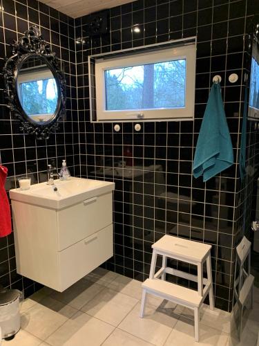 a black tiled bathroom with a sink and a stool at Skogshöjda in Tjörnarp
