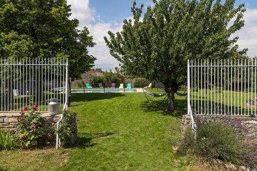 a fence with a tree and a hammock in a yard at L'enclos bleu, gîte - marais poitevin avec piscine chauffée in Chaillé-les-Marais