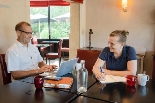 a man and a woman sitting at a table with a laptop at Brit Hotel Essentiel Cholet in Cholet