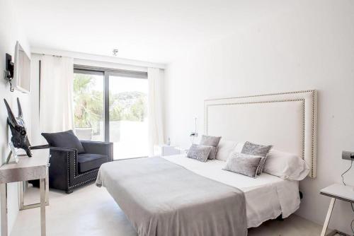 a white bedroom with a large bed and a chair at Villa La Vida in Cala Llonga