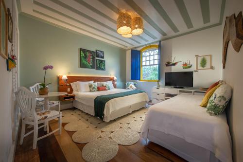 a bedroom with two beds and a desk and a tv at Sandi Hotel in Paraty