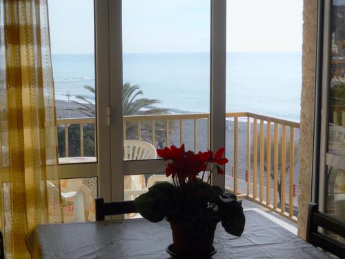 a table with a vase of flowers on a balcony with the ocean at Gaiavacanze Beach Apartment in Bordighera