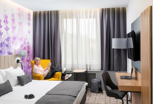 a woman sitting in a yellow chair in a hotel room at Mercure Medias Binderbubi Hotel And Spa in Mediaş