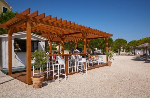 a wooden pergola with white chairs and a bar at Hotel Spongiola in Krapanj