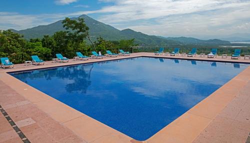 a large swimming pool with blue chairs and mountains at El Corazón Golf & Spa Resort Manzanillo in Manzanillo