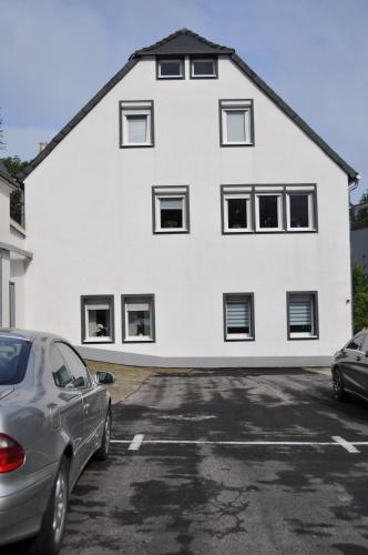 a white house with cars parked in a parking lot at Ferienwohnungen Margot in Iserlohn