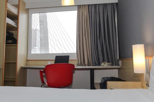 a room with a red chair and a desk and a window at ibis Sao Jose dos Campos Colinas in São José dos Campos