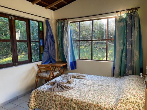 a bedroom with a bed and two windows at Solar das Mangueiras - Vale do Capão in Vale do Capao