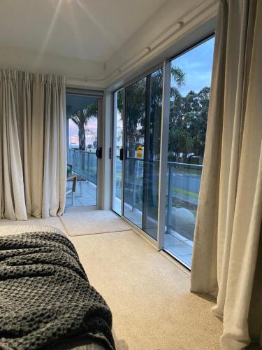 a bedroom with a bed and sliding glass doors at Modern Beach Apartment with Pool & Location in Mount Maunganui