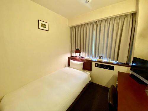 a hotel room with a white bed and a window at Smile Hotel Sasebo in Sasebo