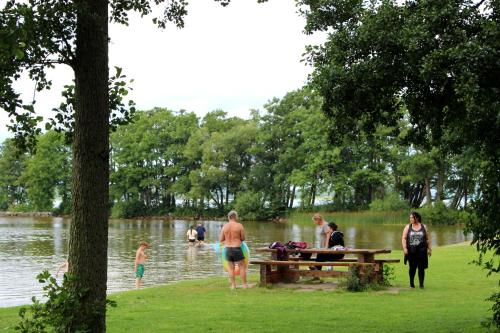 a group of people standing around a picnic table near a lake at Bromölla Camping o Vandrarhem in Bromölla