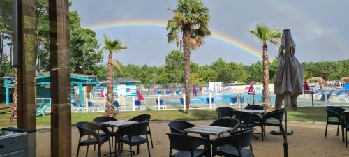 un arc-en-ciel au-dessus d'une piscine avec des tables et des chaises dans l'établissement Mobilhome 2 ch,1 salon 40m2 de Charme dans camping ***, à Saint-Julien-en-Born