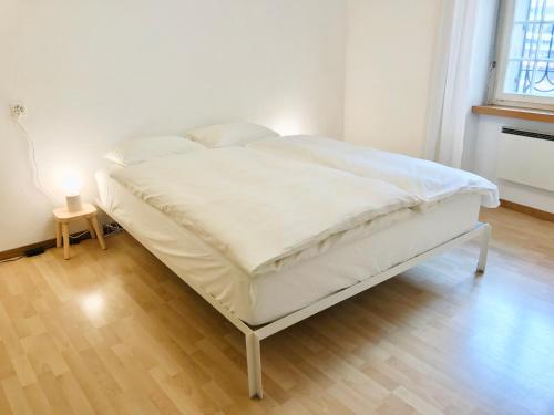 un letto bianco in una camera con pavimento in legno di Centrally Located Apartment in Poschiavo a Poschiavo