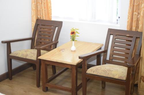 a wooden table with two chairs and a vase with flowers on it at Altius Nest Hotel in Kodaikānāl