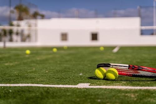 a tennis racket and three tennis balls on a court at Hotel Lanzarote Village in Puerto del Carmen