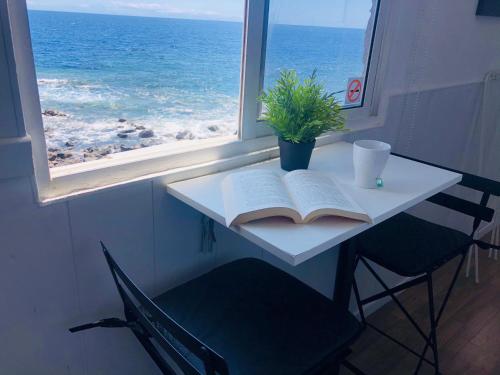 a table with an open book and a window with the ocean at Backpackers Las Eras in Santa Cruz de Tenerife