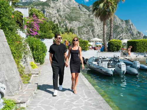a man and woman walking down a walkway next to a boat at Hotel Leonardo Da Vinci in Limone sul Garda