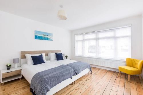 a white bedroom with a large bed and a yellow chair at Green Ridge - detached seaside home in Chichester