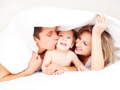 Una familia acostada en la cama con un bebé debajo de una manta. en Days Inn by Wyndham McDonough, en McDonough
