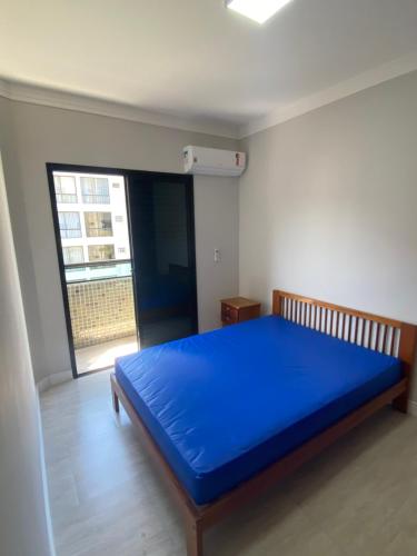 un grande letto blu in una stanza con finestra di Apto a 2 min a Pé da Praia - Edificio Monte Carmel a Guarujá