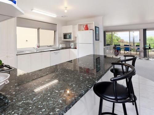 a kitchen with white cabinets and black counter chairs at Dromana Bay Views Dromana in Dromana