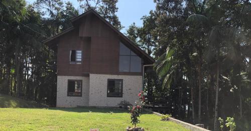a house on a grassy field next to trees at Casa de campo Rosa dos ventos in Rodeio