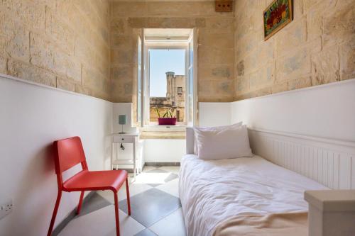 um quarto com uma cama e uma cadeira vermelha em Valletta Collection - St Pauls Apartment em Valletta