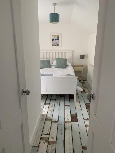 a bedroom with a white bed and a wooden floor at Hobbes Cottage, pets allowed in Tenby