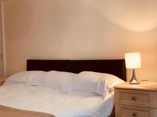 a bed with white sheets and a lamp on a nightstand at De Parys Guest House - Fully Airconditioned in Bedford