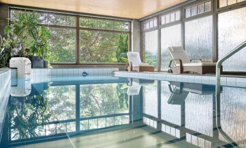 einen Pool mit zwei Stühlen in einem Zimmer mit Fenstern in der Unterkunft Schlossberghotel Oberhof in Oberhof