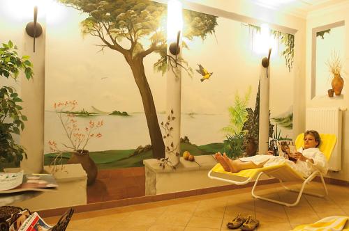 a woman sitting in a chair in a room with a tree at Ferienanlage - Zum See & Hotel in Plau am See