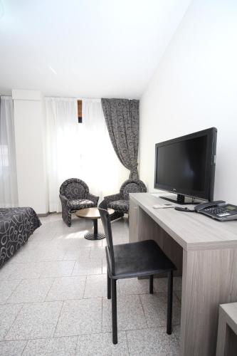 a living room with a television and a desk with a chair at Hotel Croce Di Malta in Novara