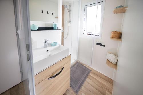 La salle de bains blanche est pourvue d'un lavabo et d'une douche. dans l'établissement Mobil home 3 chambres 2 salles de bains au camping 4 étoiles MH276 aux charmettes, aux Mathes