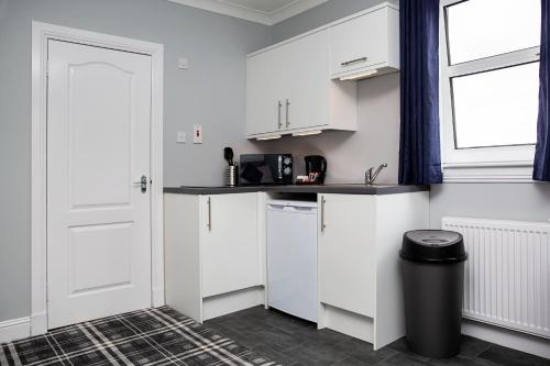 a small kitchen with white cabinets and a window at St Andrews Guest House in Irvine